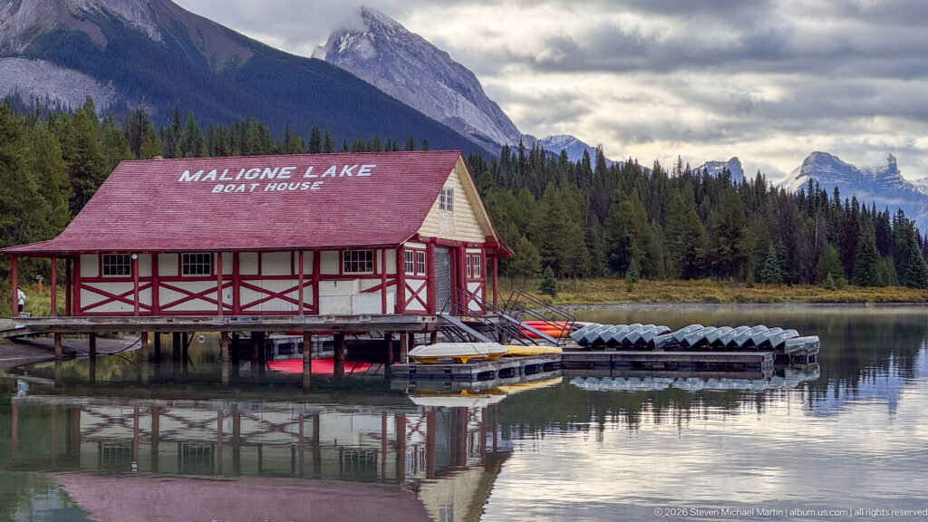 A closer view shows the red-and-cream Maligne Lake Boat House over water, adjacent canoe racks, forest, and mountain slopes