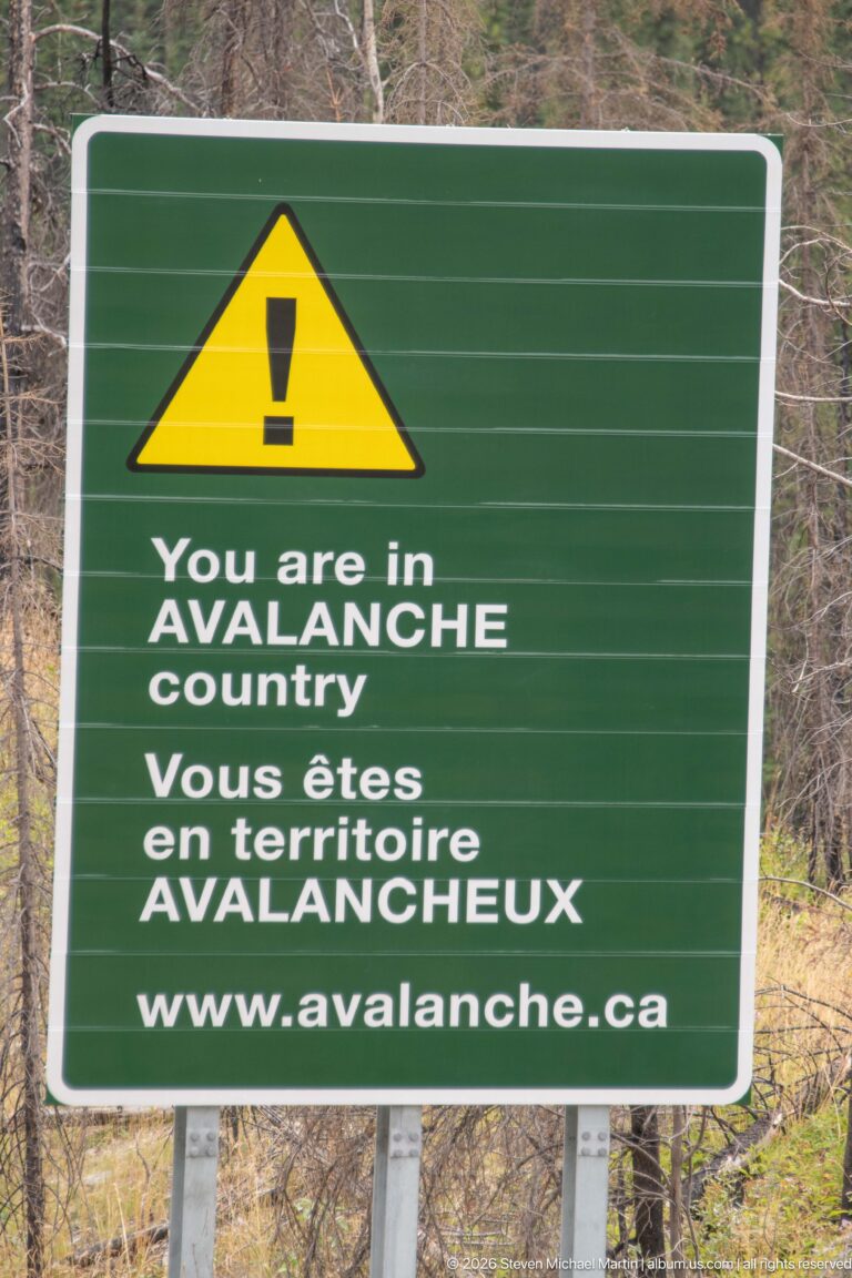 Green bilingual avalanche warning sign with yellow caution symbol stating “You are in AVALANCHE country.”