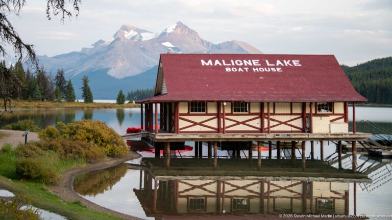 Maligne Lake Boathouse with its name painted on a red roof, reflected in still water beside docks.