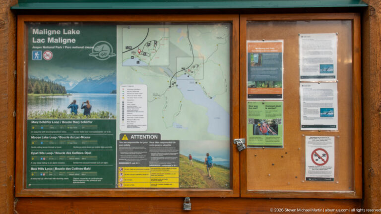 A wooden information case displays a Maligne Lake trail map, route information, notices, and visitor guidance