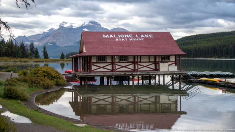 The red-roofed Maligne Lake Boathouse stands over the water, its timber-framed walls reflected below