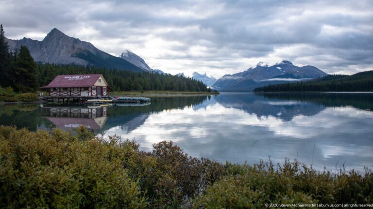 The Maligne Lake Boathouse sits at left across calm reflective water with mountains lining the lake axis