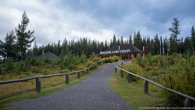A paved path with rustic railings rises toward the clearly signed Maligne Lake Chalet