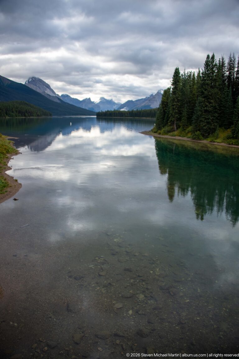 Clear shallow water and a forested shoreline lead toward distant mountain ridges