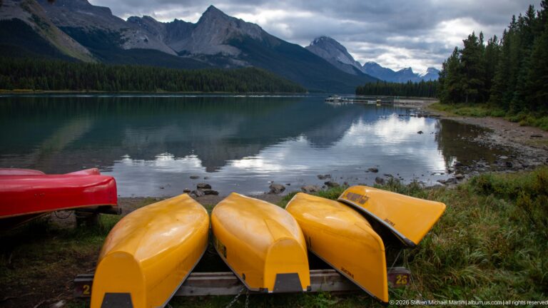 Yellow canoes rest at the shoreline with Maligne Lake and steep mountain ridges beyond