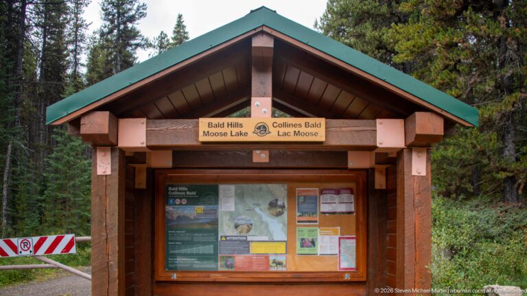 Timber trail kiosk with green roof and bilingual signs for Bald Hills and Moose Lake.