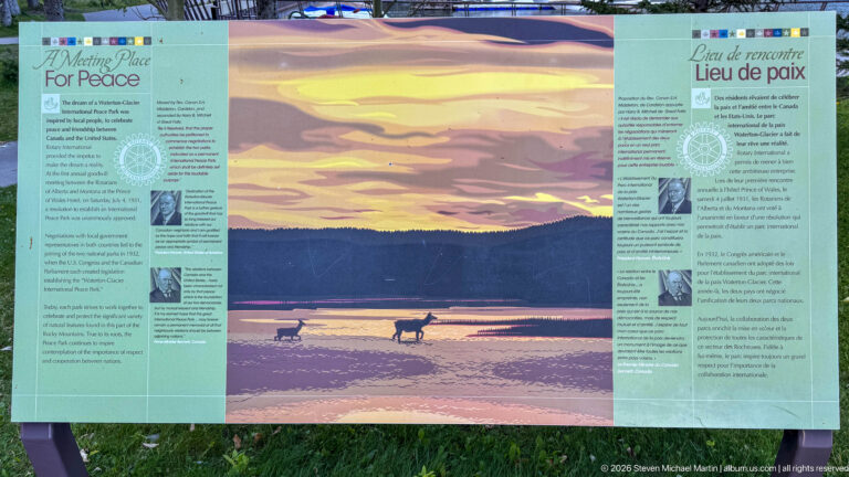 Bilingual Place of peace panel with two ungulates in shallow water against a glowing mountain landscape, flanked by text columns.