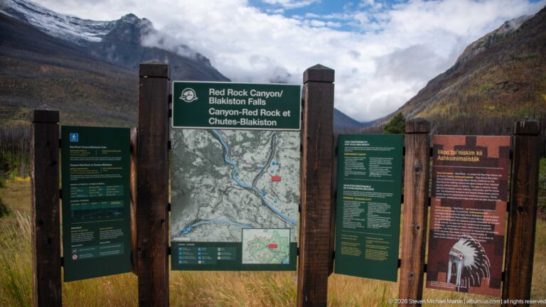 Timber-framed Red Rock Canyon and Blakiston Falls trailhead display with map and information panels beneath cloud-covered mountains.