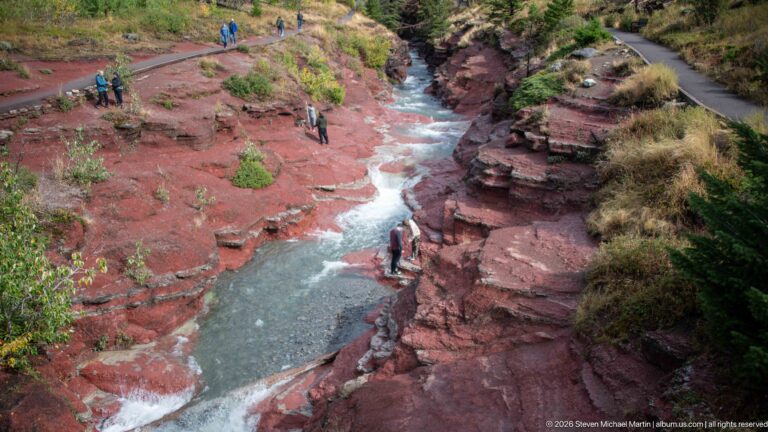 Elevated view of a stream winding through red-rock canyon walls beside a paved path on the rim.
