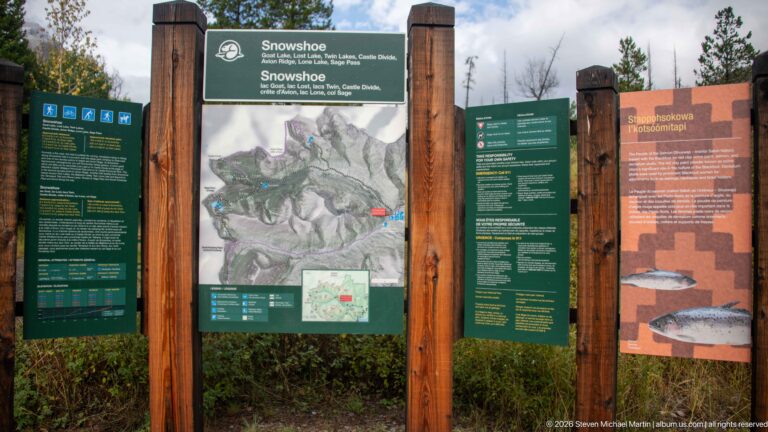 Snowshoe trailhead board with central topographic map, green bilingual information panels, and an orange bull-trout interpretive panel.