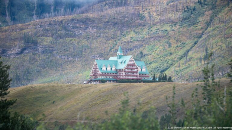 Distant Prince of Wales Hotel with green roof and red-and-cream façade on a ridge below a broad fire-altered mountain slope.