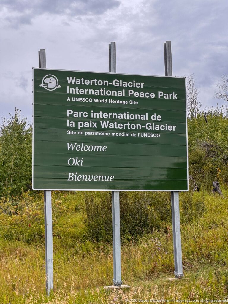 Green bilingual Waterton-Glacier International Peace Park sign identifying the area as a UNESCO World Heritage Site.