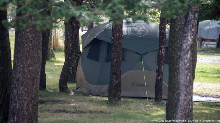 Large green-and-gray cabin tent pitched among mature trees on a grassy Waterton Lakes campground site.