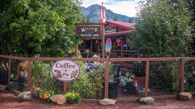 Welch’s Chocolate Shop behind a rustic fence and flower garden, with a Canadian flag and round Coffee & Pie sign.