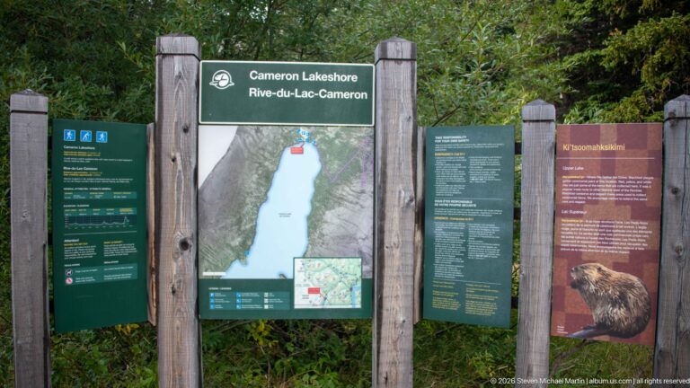 Cameron Lakeshore information board with lake map, visitor information, trail details, and a bear-themed interpretive panel.