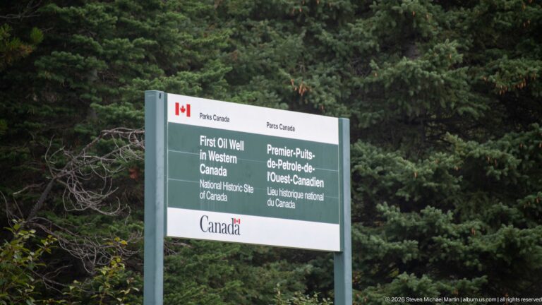Parks Canada sign identifying First Oil Well in Western Canada National Historic Site in English and French against evergreen forest.