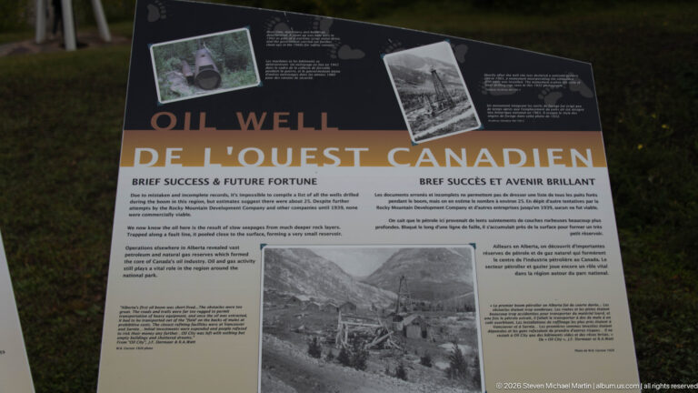 Bilingual oil-well interpretive panel with archival photographs of drilling structures and a mountain valley.