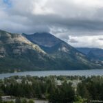 Waterton townsite among trees below Upper Waterton Lake, with steep mountains enclosing the valley under heavy clouds.