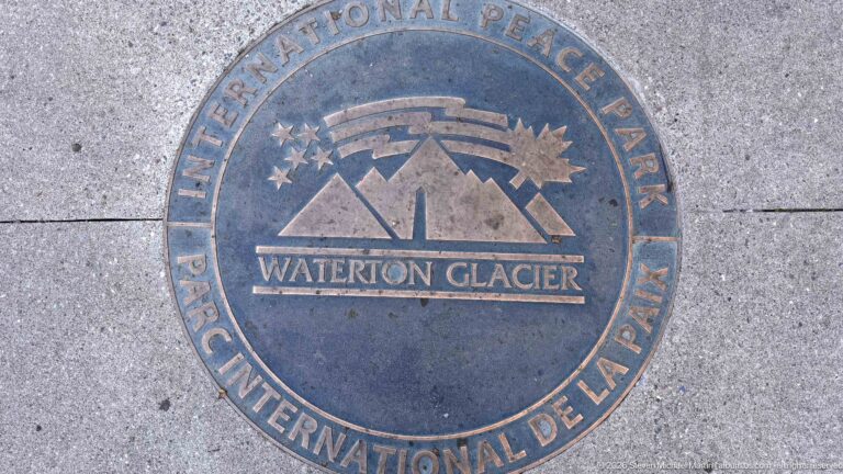 Circular Waterton-Glacier International Peace Park medallion set into pavement with mountains, stars, and bilingual lettering.
