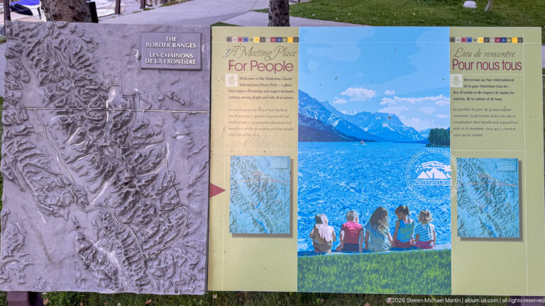 Bilingual A Meeting Place For People panel with lake-and-mountain artwork, maps, and an adjacent sculpted relief panel.