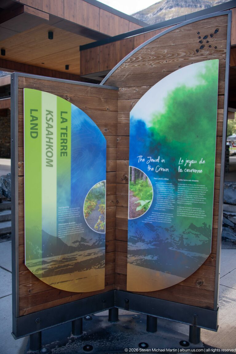 Curved wooden outdoor exhibit with colorful bilingual panels about land, water, and The Jewel in the Crown.