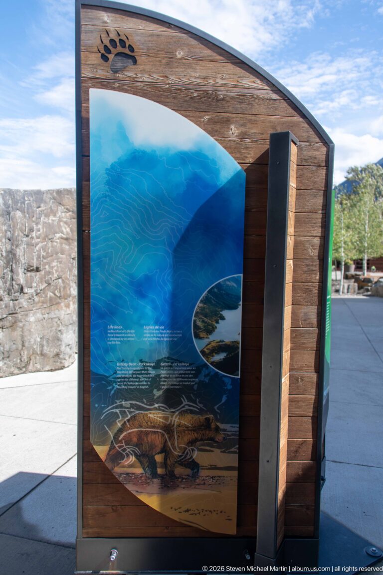 Curved wood-framed outdoor panel with blue water graphics, contour lines, and circular landscape inset.
