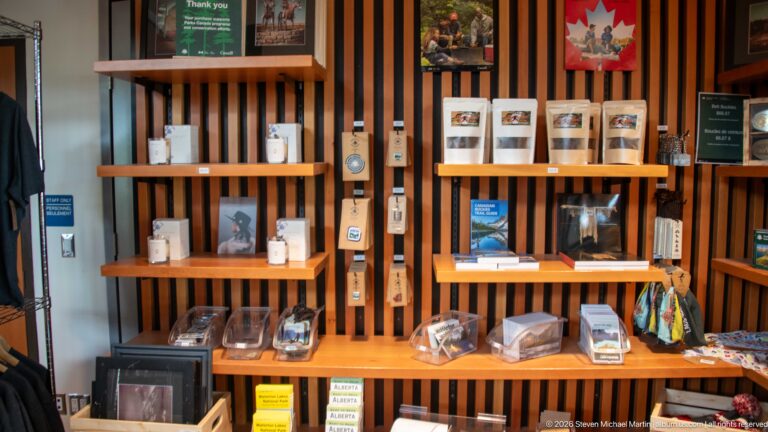 Wooden visitor centre shop shelves displaying books, cards, souvenirs, boxed items, and Parks-related merchandise.