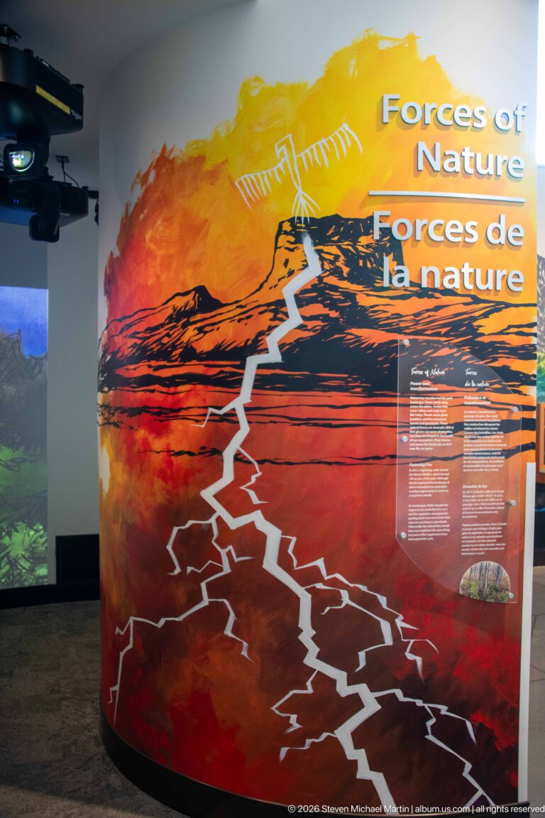 Curved orange-red bilingual “Forces of Nature” wall with mountain silhouette, jagged white graphic, and text panels.