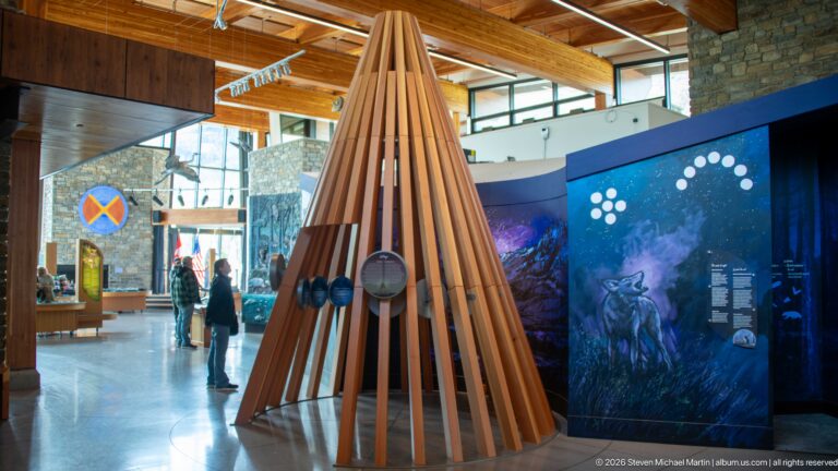 Tall cone of vertical wooden slats with circular interactive elements in bright visitor centre gallery.