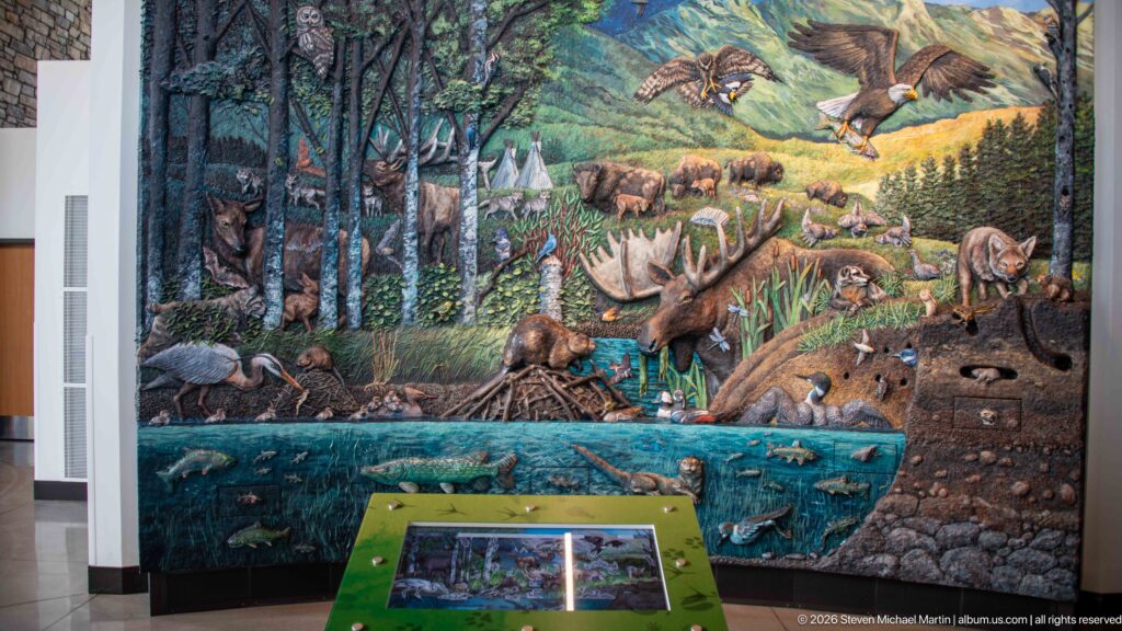 Large wildlife ecosystem mural with forest animals, birds, mammals, fish, and an interactive station in front.