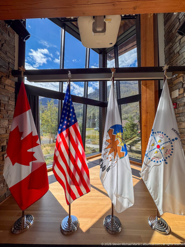 Four tabletop flags, including Canada and the United States, displayed before timber beams and mountain-facing windows.