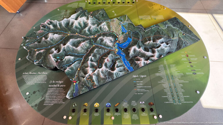 Overhead view of a circular interactive relief map with raised mountains, lakes, legends, and push buttons.