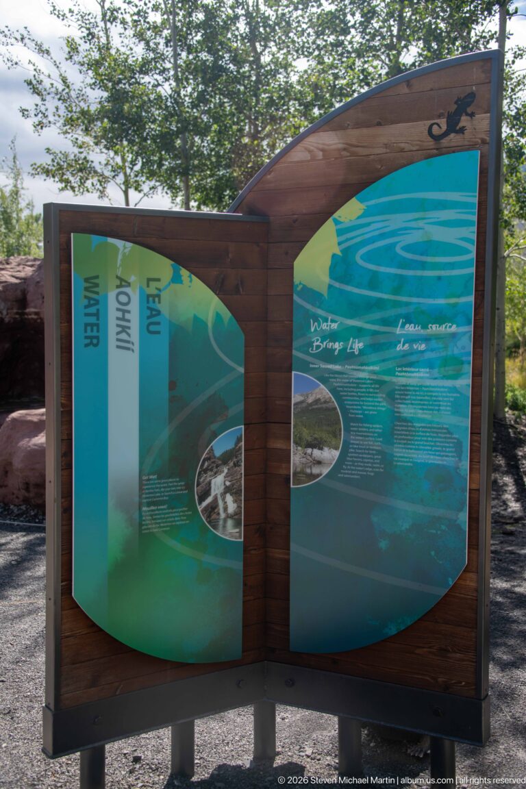 Curved wooden outdoor interpretive display with blue-green bilingual panels about water and inset landscape photographs.