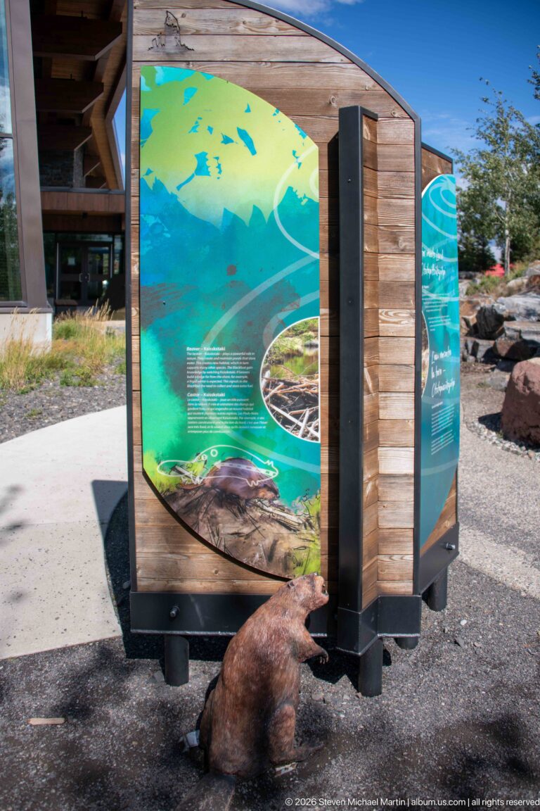 Beaver sculpture at the base of a colorful outdoor interpretive panel beside the visitor center.