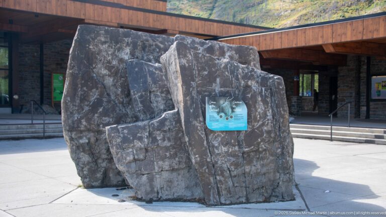Large split-rock interpretive feature with a small panel in the paved visitor centre plaza.