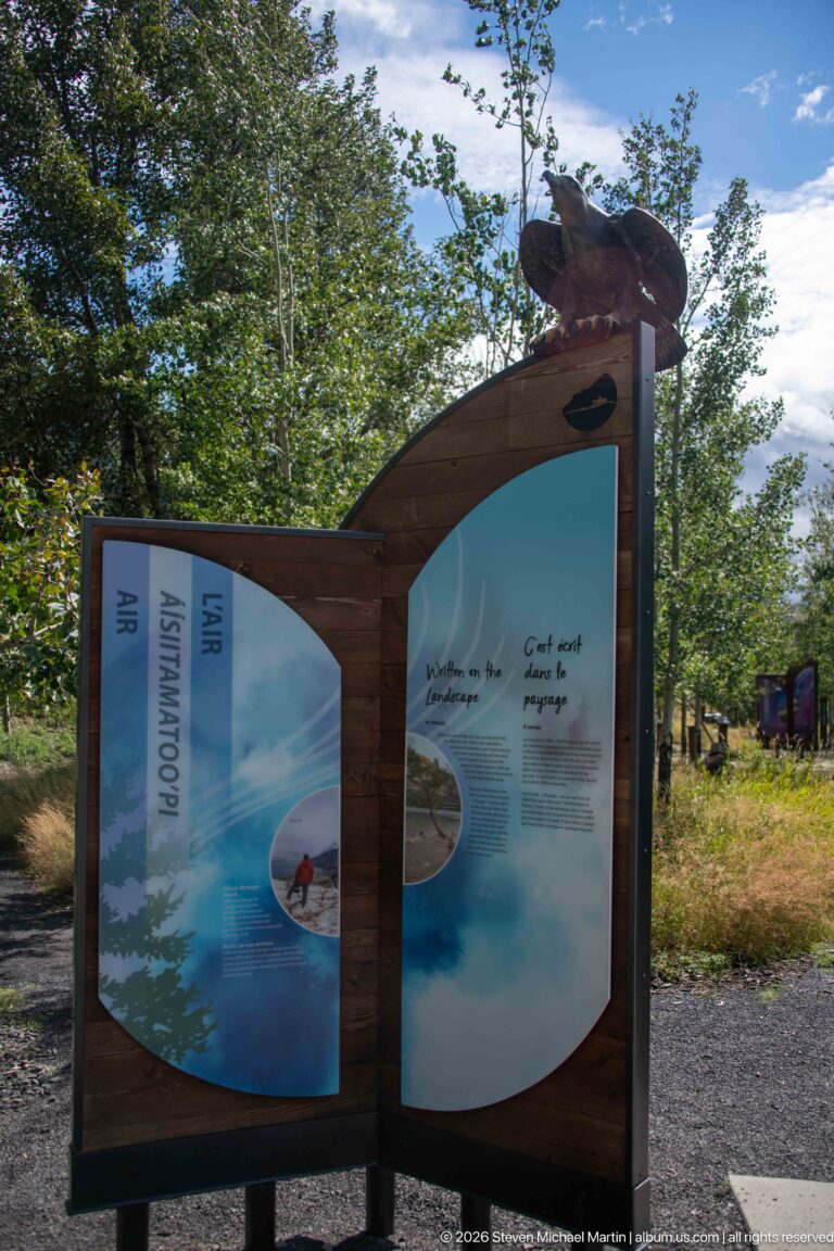Curved wooden interpretive panel with pale blue air graphics, vertical ASPEN and AIR labels, and a bird sculpture on top.