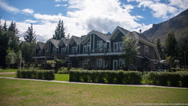 Long two-story lodge building with repeated steep gables and balconies facing a lawn beneath mountain slopes.