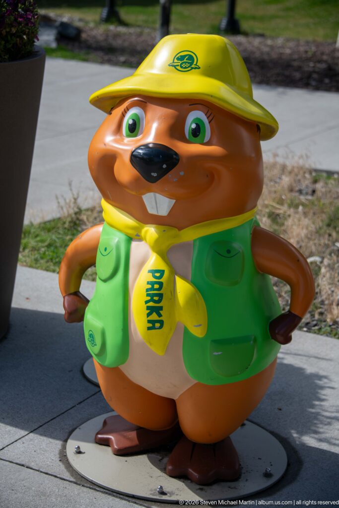 Close view of smiling beaver mascot in yellow ranger hat and green vest on a circular base.