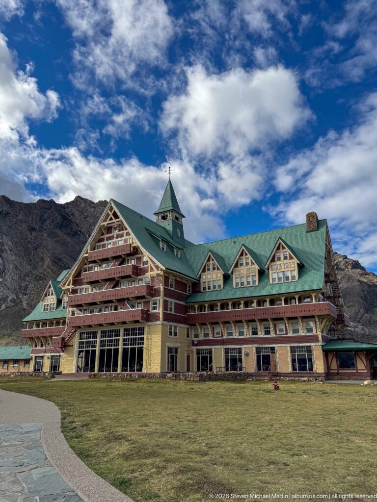 Broad front view of Prince of Wales Hotel across a lawn, showing green roofs, gables, balconies, and large lower windows.