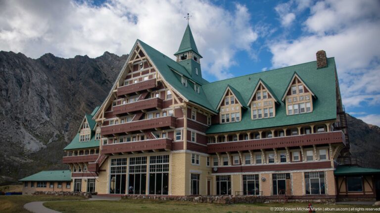 Three-quarter exterior view of Prince of Wales Hotel with tall gable, stacked balconies, green roof, and mountain behind.