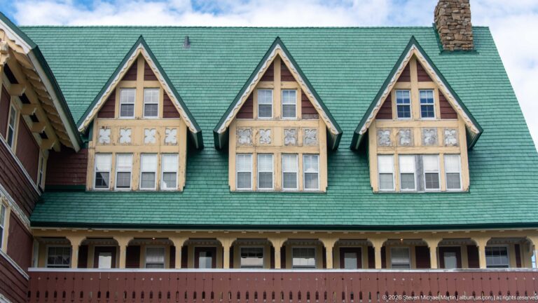 Three projecting hotel gables with multi-pane windows, pale timber detailing, patterned panels, and a green shingled roof.