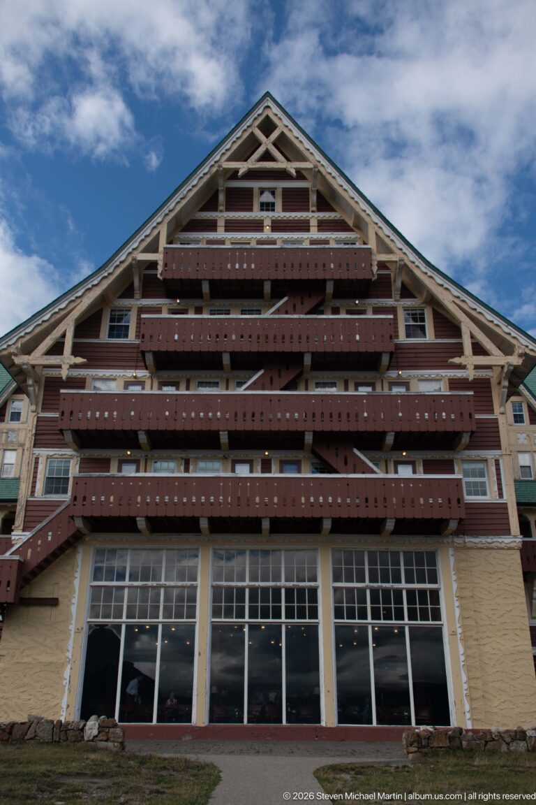 Low-angle view of a broad gabled hotel façade with stacked red-brown balconies, exposed roof framing, and large ground-floor windows.