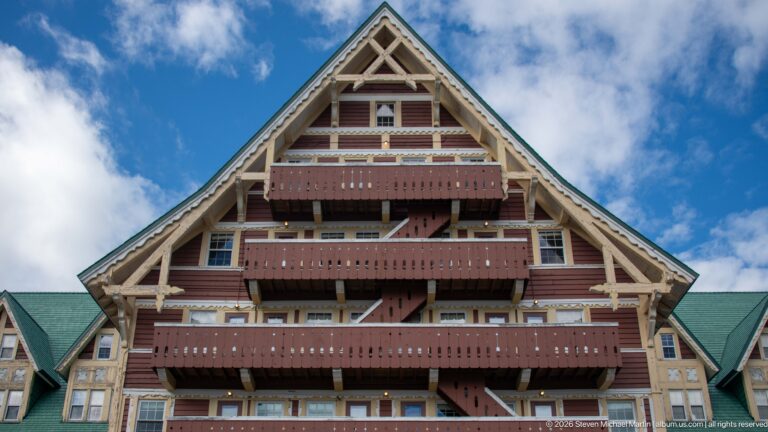 Large triangular hotel gable with stacked red balconies, pale timber framing, windows, and green roof edges.