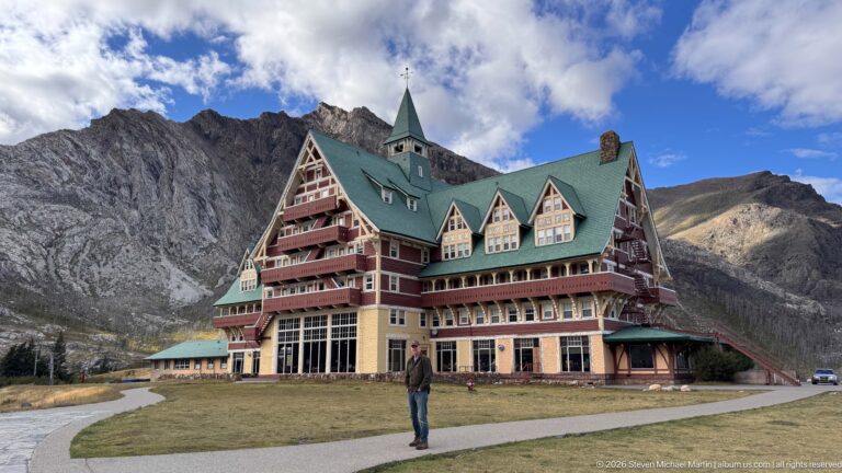 Prince of Wales Hotel viewed across lawn with a visitor in front and jagged gray mountain ridge behind.