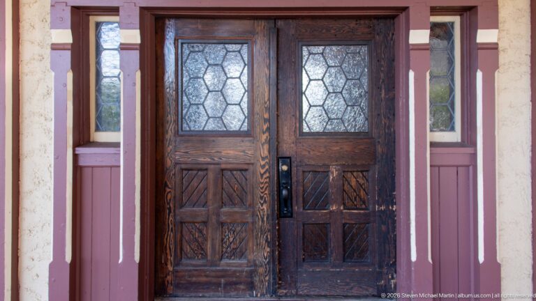Dark wooden double doors with carved geometric panels and leaded glass, framed by red-and-cream hotel trim.