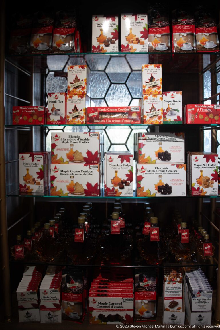 Dark cabinet filled with boxed Canadian maple-themed products and small souvenirs, backed by leaded glass.