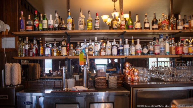 Wood-paneled hotel bar stocked with liquor bottles, glassware, taps, and stainless-steel service equipment.