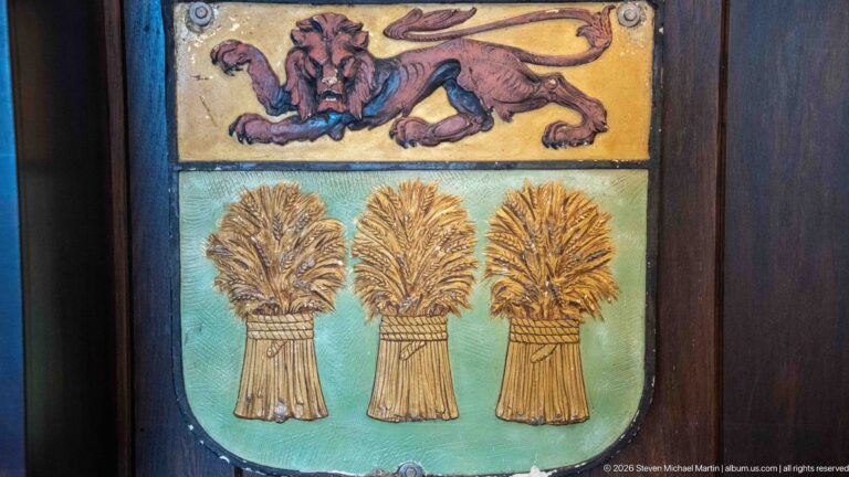 Painted decorative panel with a reclining lion above a turquoise shield bearing three golden wheat sheaves.