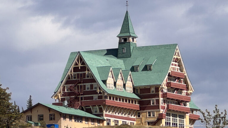 Oblique view of the Prince of Wales Hotel with green roofs, red siding, gables, balconies, and pale lower walls.