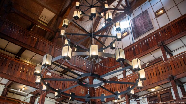 Upward view of a tall timber lobby with carved balconies and multiple large circular chandeliers suspended from exposed roof framing.